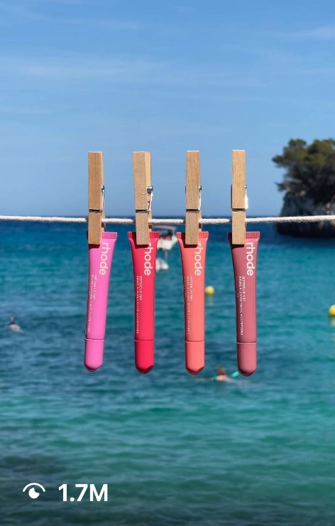 Lipsticks displayed on a clothesline, with a serene water backdrop, featured in an Instagram post by Rhode.